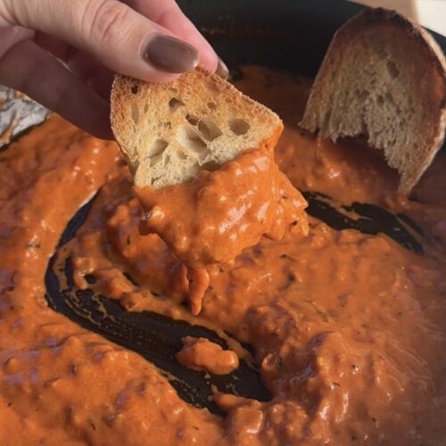 Front view of toasted bread being dipped in spicy red sauce from the pan.