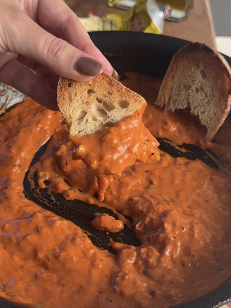 Front view of toasted bread being dipped in spicy red sauce from the pan.