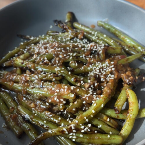A bowl of green beans topped with a pan sauce and sesame seeds