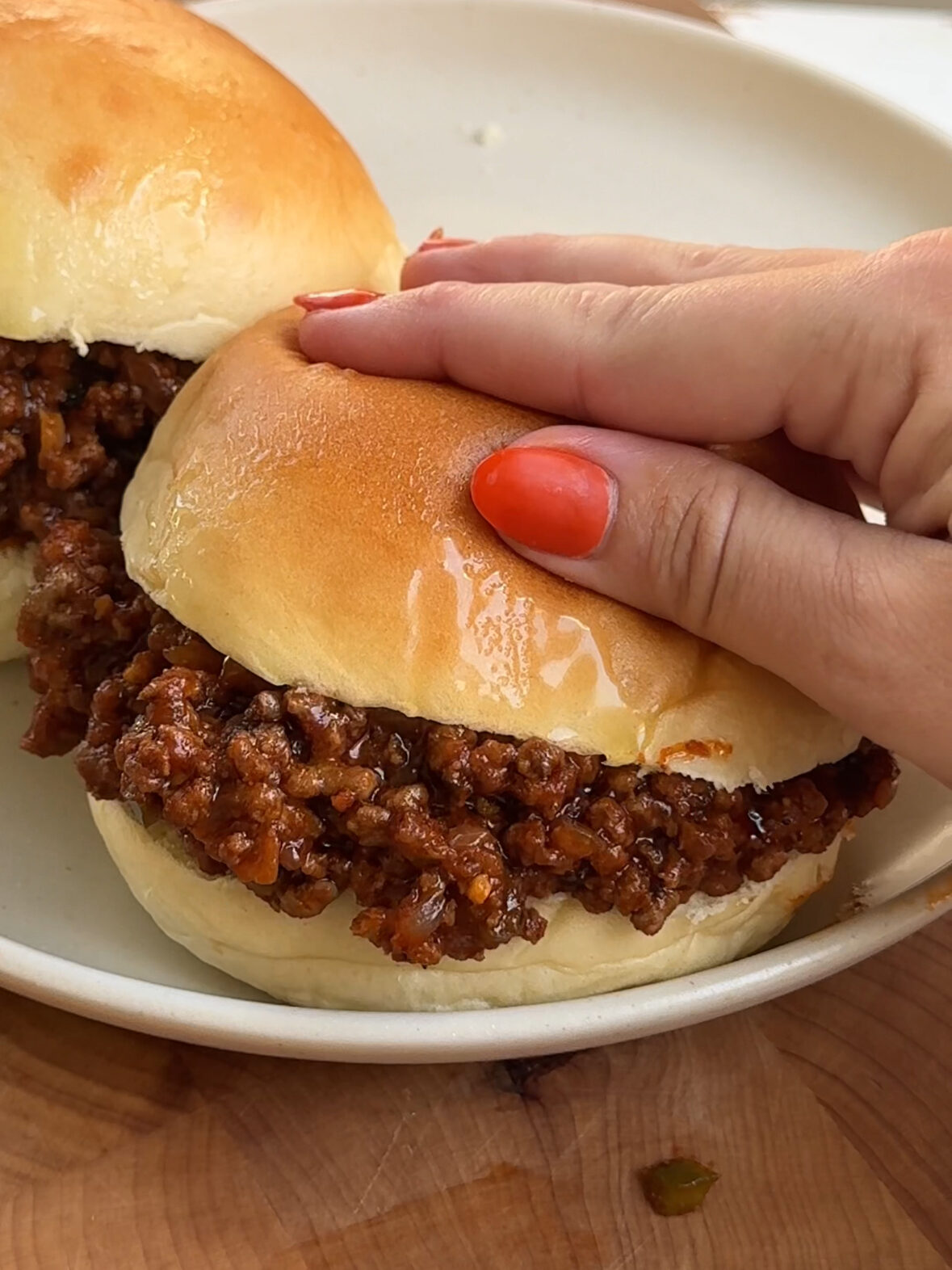 Spicy sloppy joes on a hamburger bun with a hand closing the bun