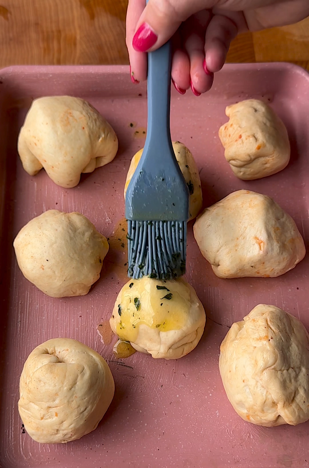 brushing the pizza dough balls with sauce on top of a pink baking sheet