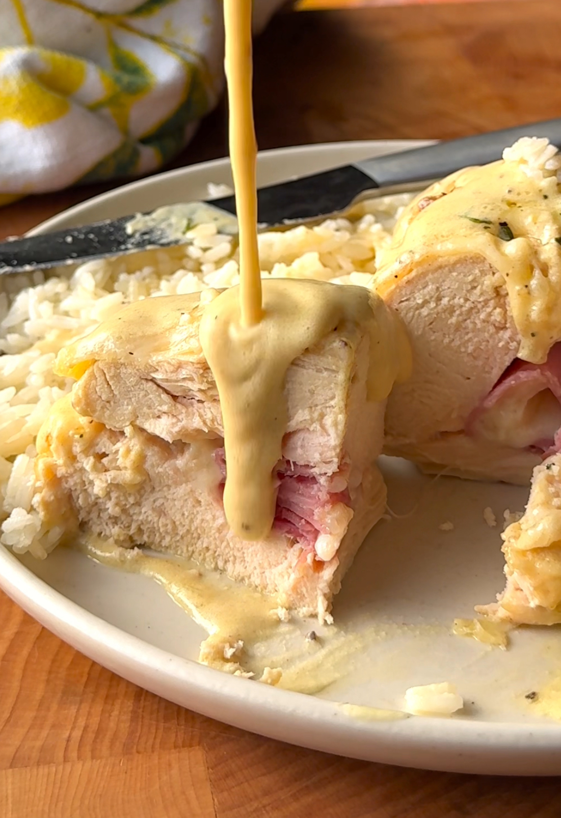 slice of chicken cordon bleu on a plate with rice with a sauce being poured over