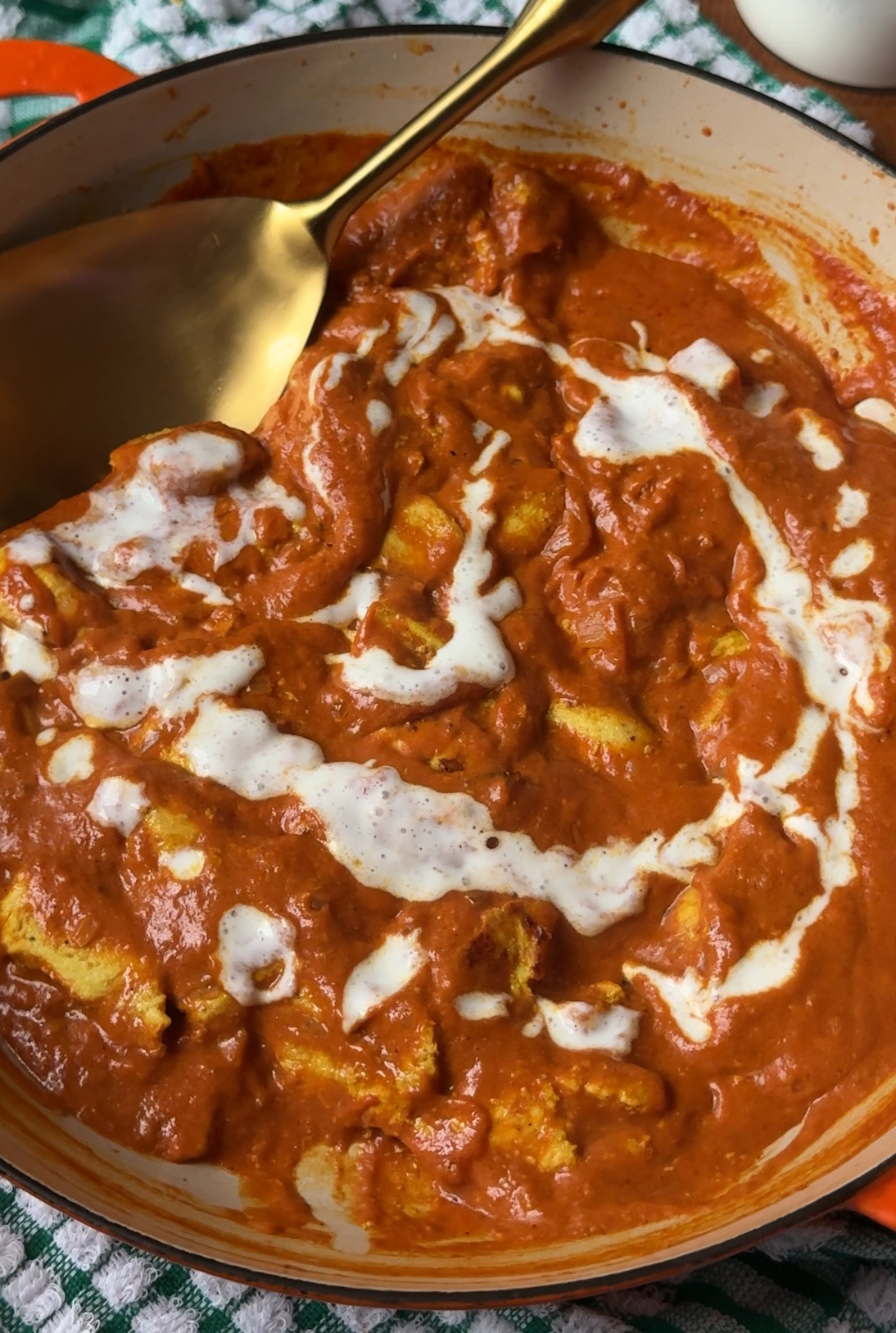 chicken tikka masala in a pan with yogurt sauce drizzled on top with a gold spoon