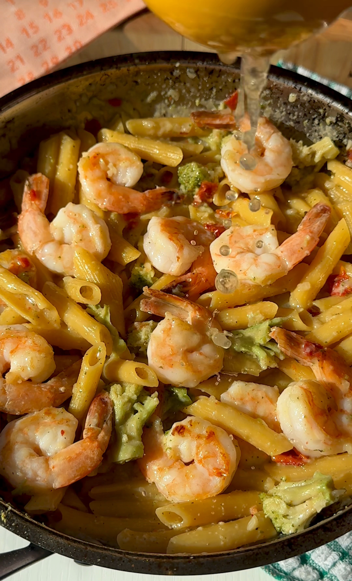 a pan with penne pasta broccoli and shrimp pouring lemon juice on top
