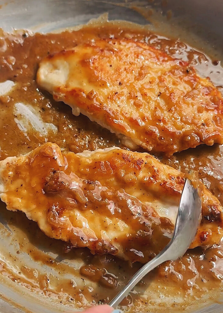 spooning marsala sauce onto chicken breast in the pan