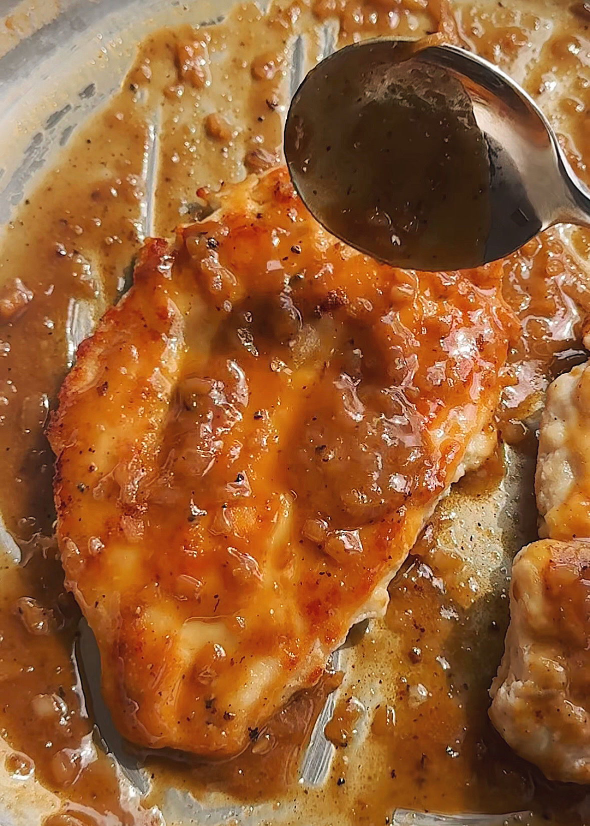 spooning marsala sauce onto one chicken breast