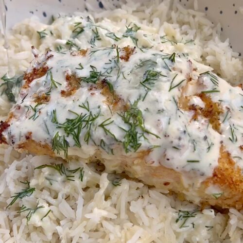 dill yogurt sauce on top of salmon sitting on white rice in a bowl